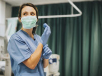 Female nurse with a mask putting on gloves