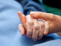 A young hand touches and holds an old wrinkled hand